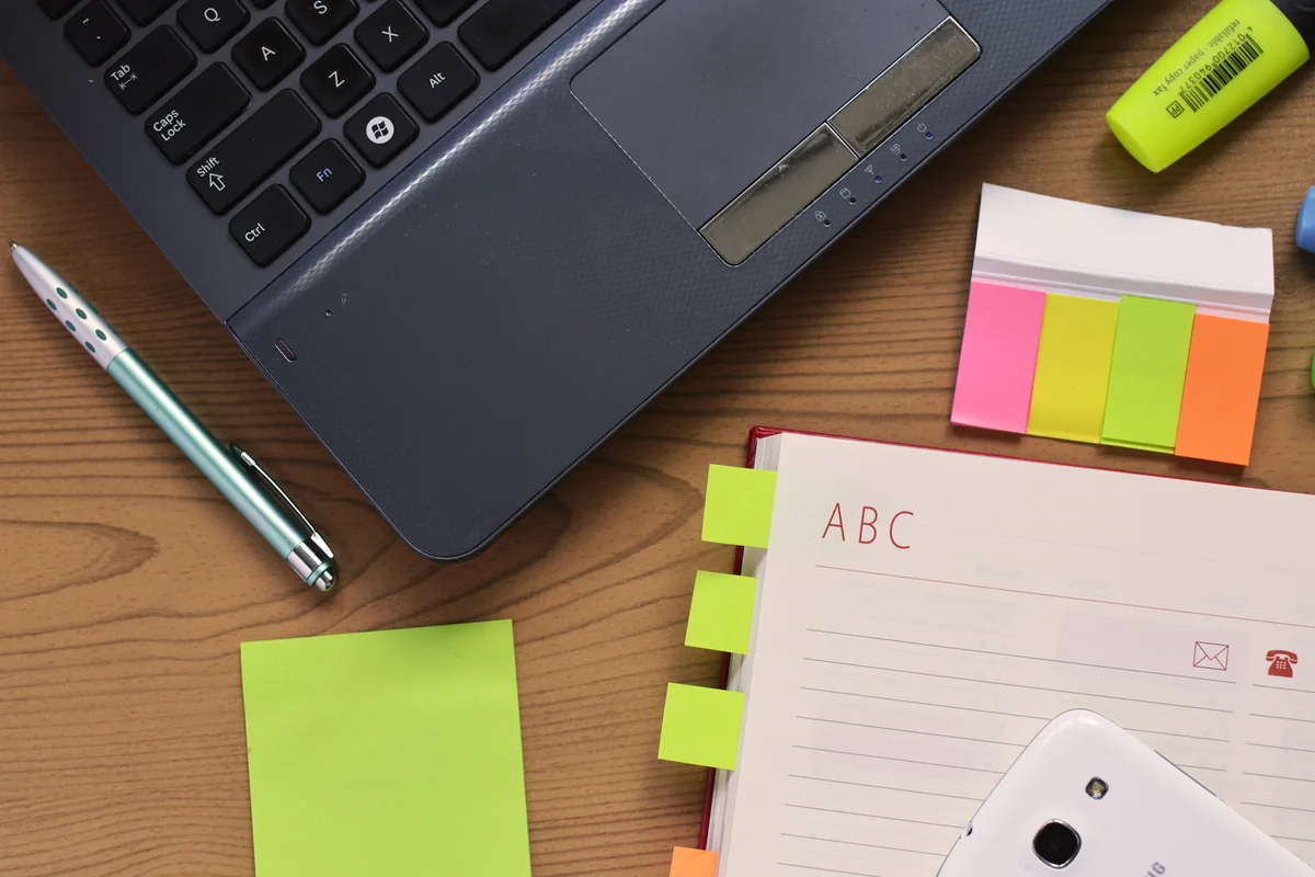 Laptop mit Notizbuch und Stift – illustrative Darstellung eines Arbeitsplatzes, nicht ein konkretes Projekt oder Büro.